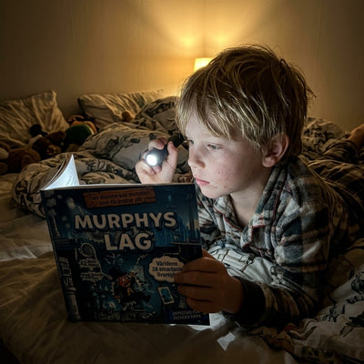 Pojke läser Murphys lag med ficklampa i sängen